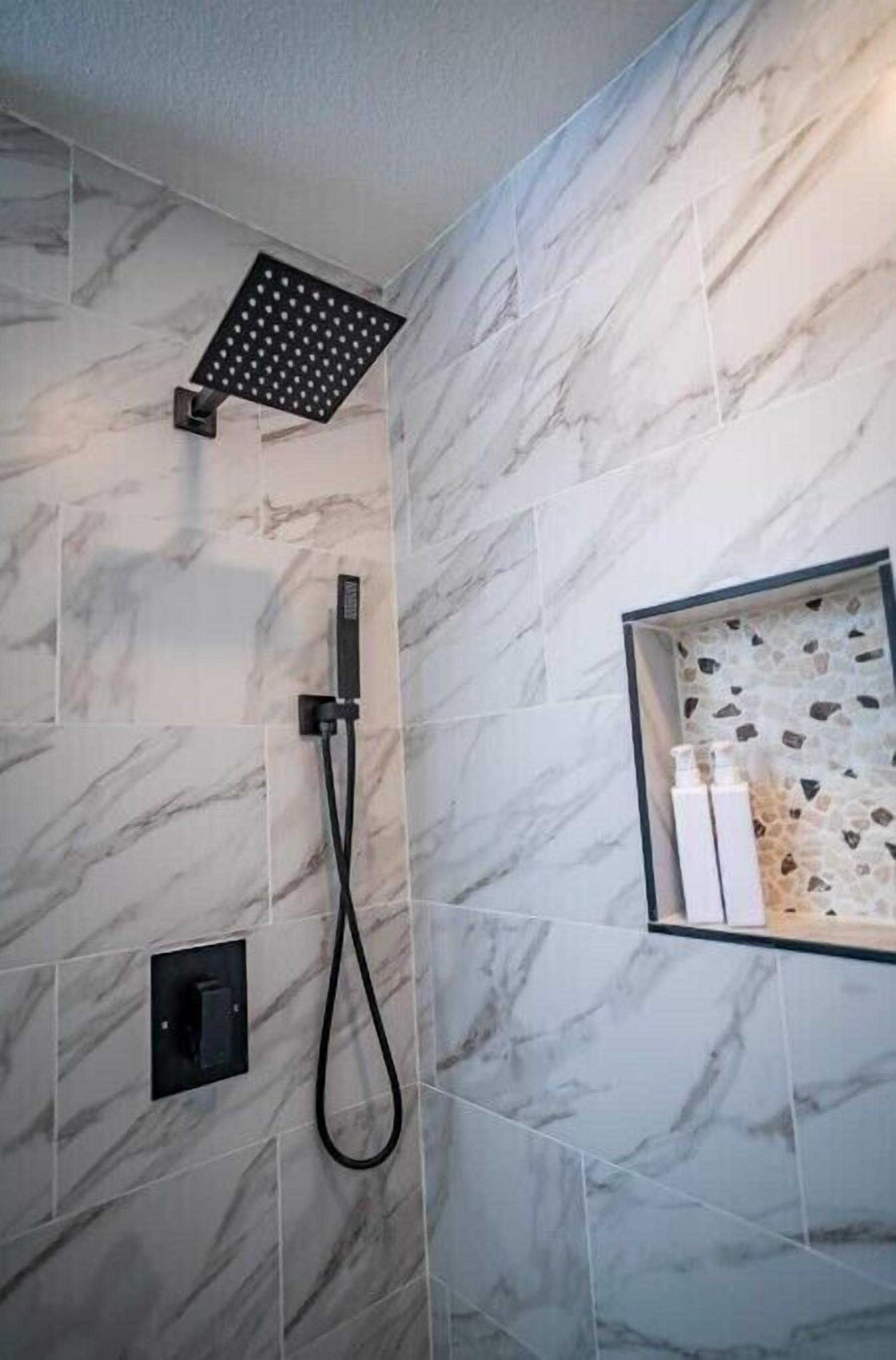 Un baño moderno con ducha, azulejos de mármol, un estante empotrado con artículos de aseo y un panel de control.