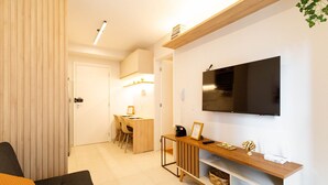 A modern living room with a flat-screen TV mounted on the wall, a wooden coffee table, and a seating area with a sofa and chairs. - Studio Laguna (São Paulo)
