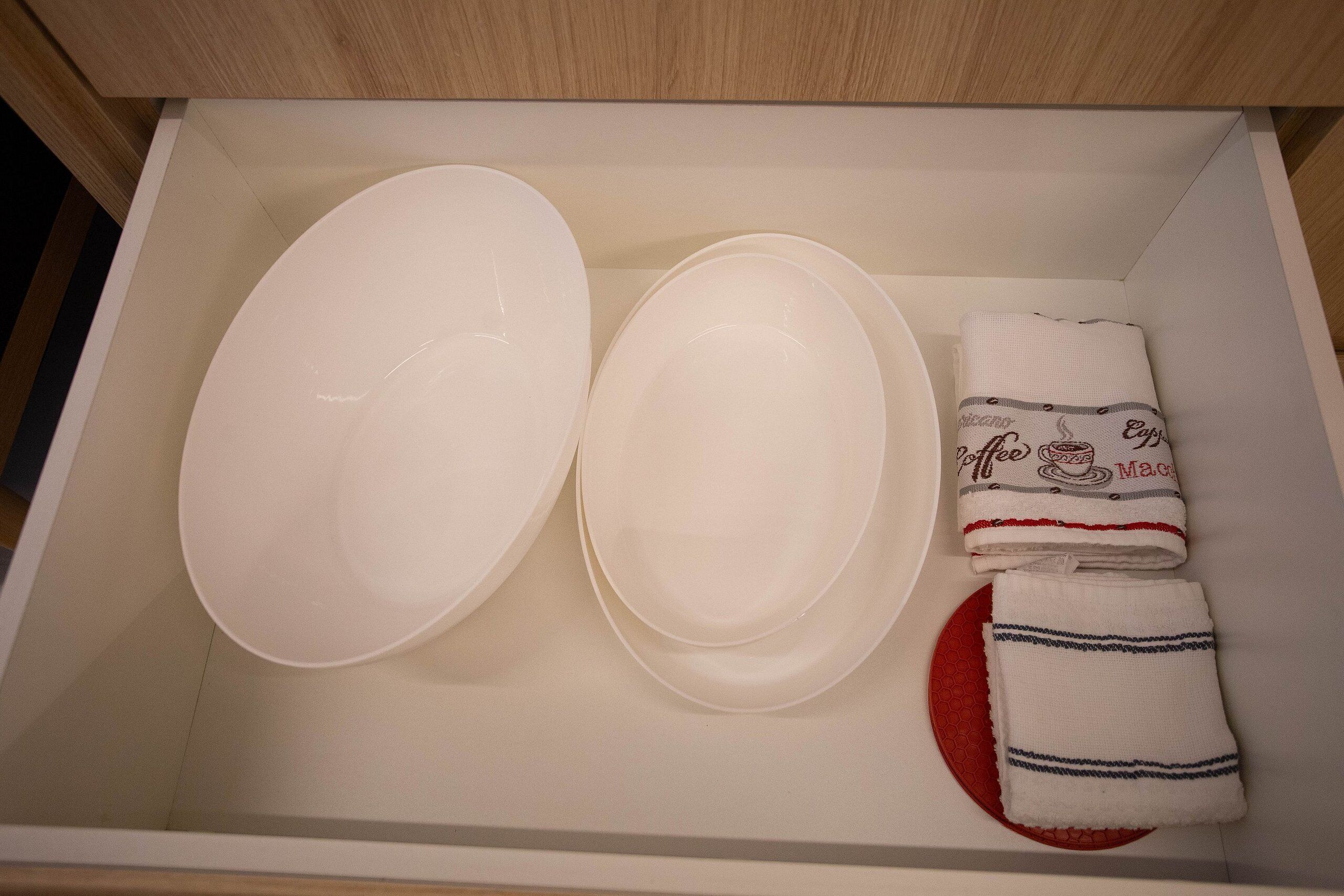 A drawer containing white plates, a folded white cloth with a coffee pattern, and a red circular object.