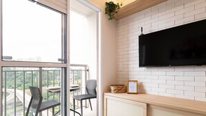 A balcony with a table and chairs, a TV mounted on a brick wall, and a view of a cityscape. - Studio Laguna (São Paulo)