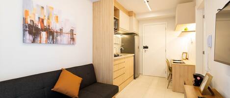 Un apartamento moderno con un sofá de color gris oscuro, una mesa de comedor de madera y una cocina con armarios de madera y un refrigerador de acero inoxidable.