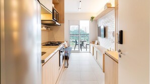 A modern kitchen with a built-in stove, microwave, and oven. There is a dining area with a table and chairs, and a large window offering a view of the city. - Studio Laguna (São Paulo)