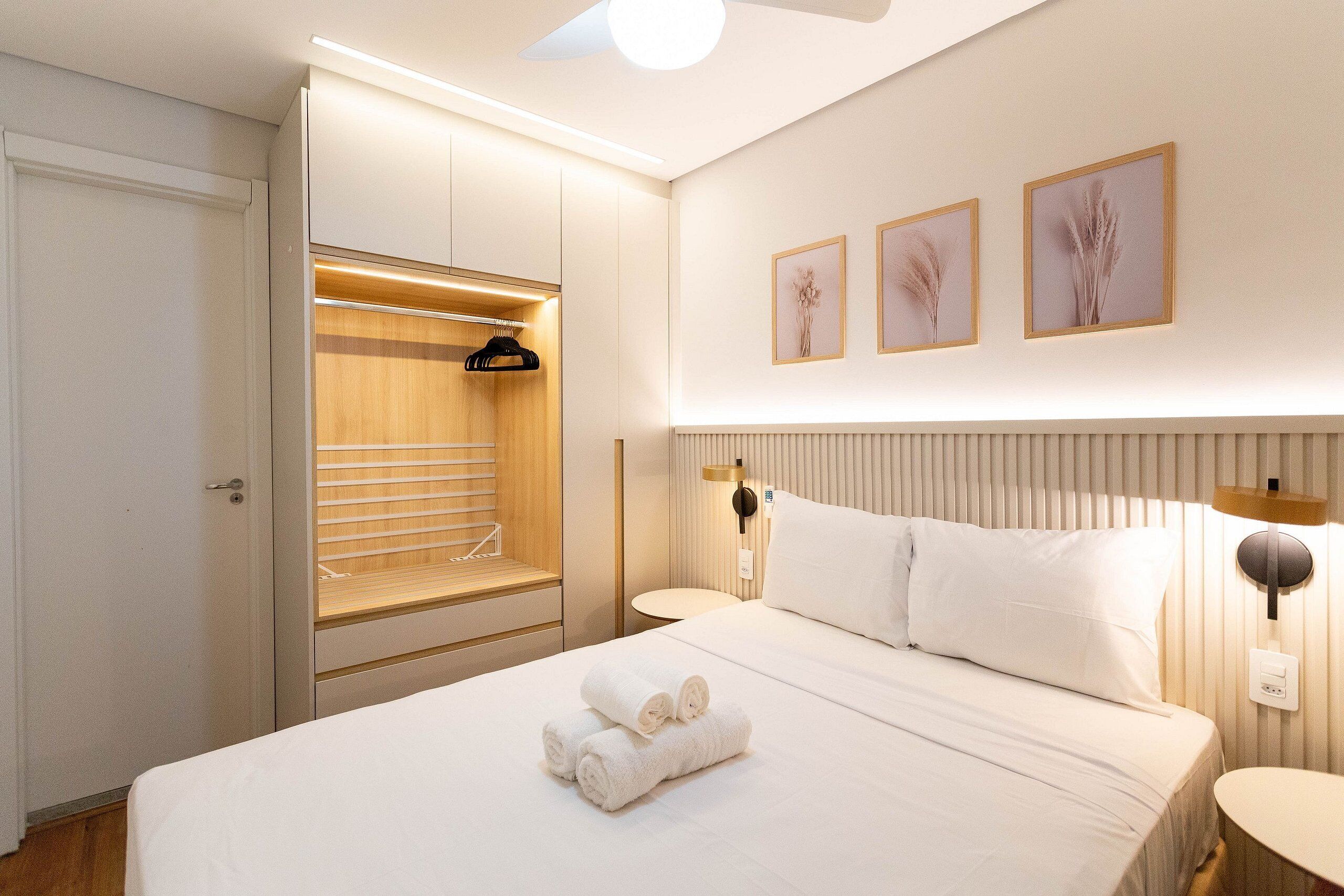 Une chambre d’hôtel moderne avec un lit bien fait, un dressing et une table de chevet avec une lampe.