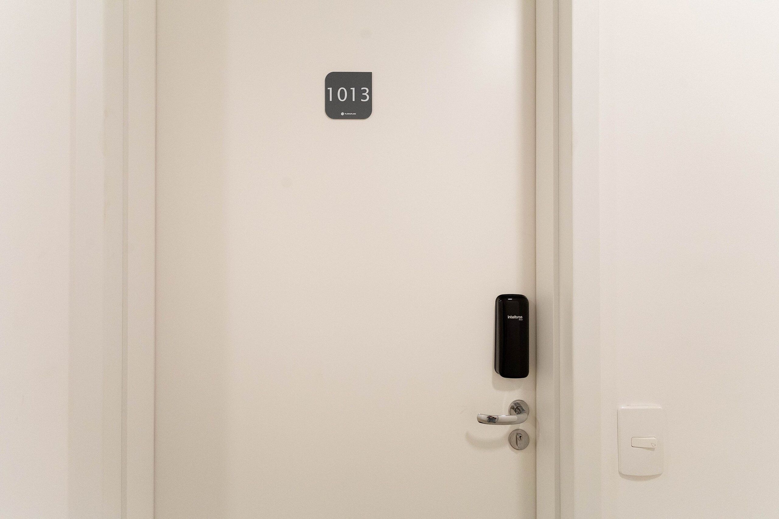 Una puerta con cerradura electrónica, una mirilla y una placa con el número de la habitación.