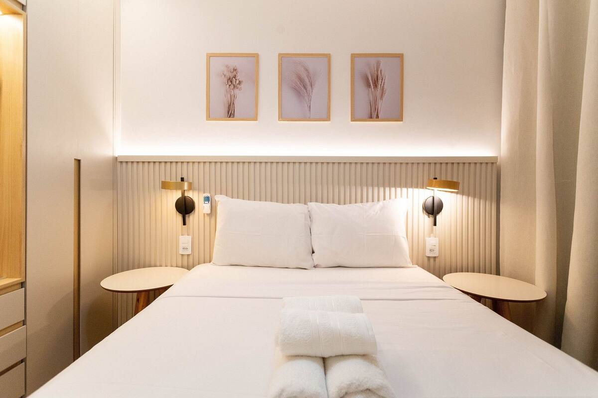 A hotel room with a large bed, two bedside tables, a wall-mounted lamp, and three framed pictures on the wall.
