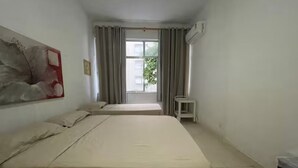 A hotel room with two beds, a window with curtains, a small table, and an air conditioning unit. - SuhcasaCopacabana 50 Ocean View (Rio de Janeiro)