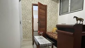 A room with a bed, a small table with a tablecloth, a wooden bench, a wall-mounted shelf with a horse figurine, and a door leading to another room. - SuhcasaCopacabana 50 Ocean View (Rio de Janeiro)