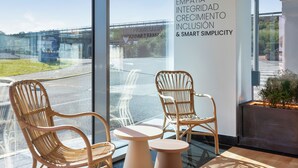 A modern interior with wicker chairs and a glass table, a large window with a view of a bridge and greenery, and a wall with motivational words.