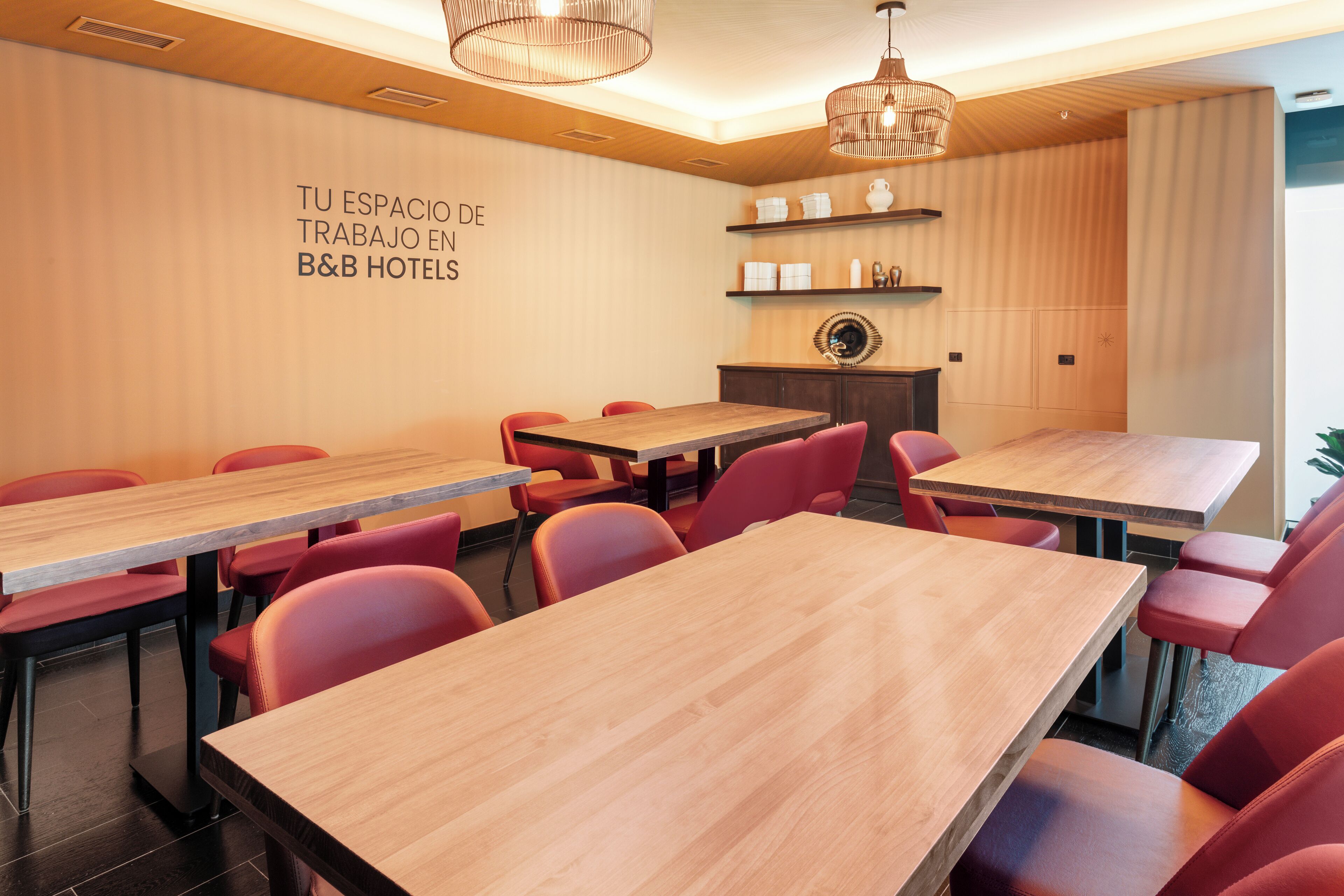 Un espacio de trabajo en un hotel con varias mesas y sillas, paredes de madera y estanterías con utensilios de cocina.