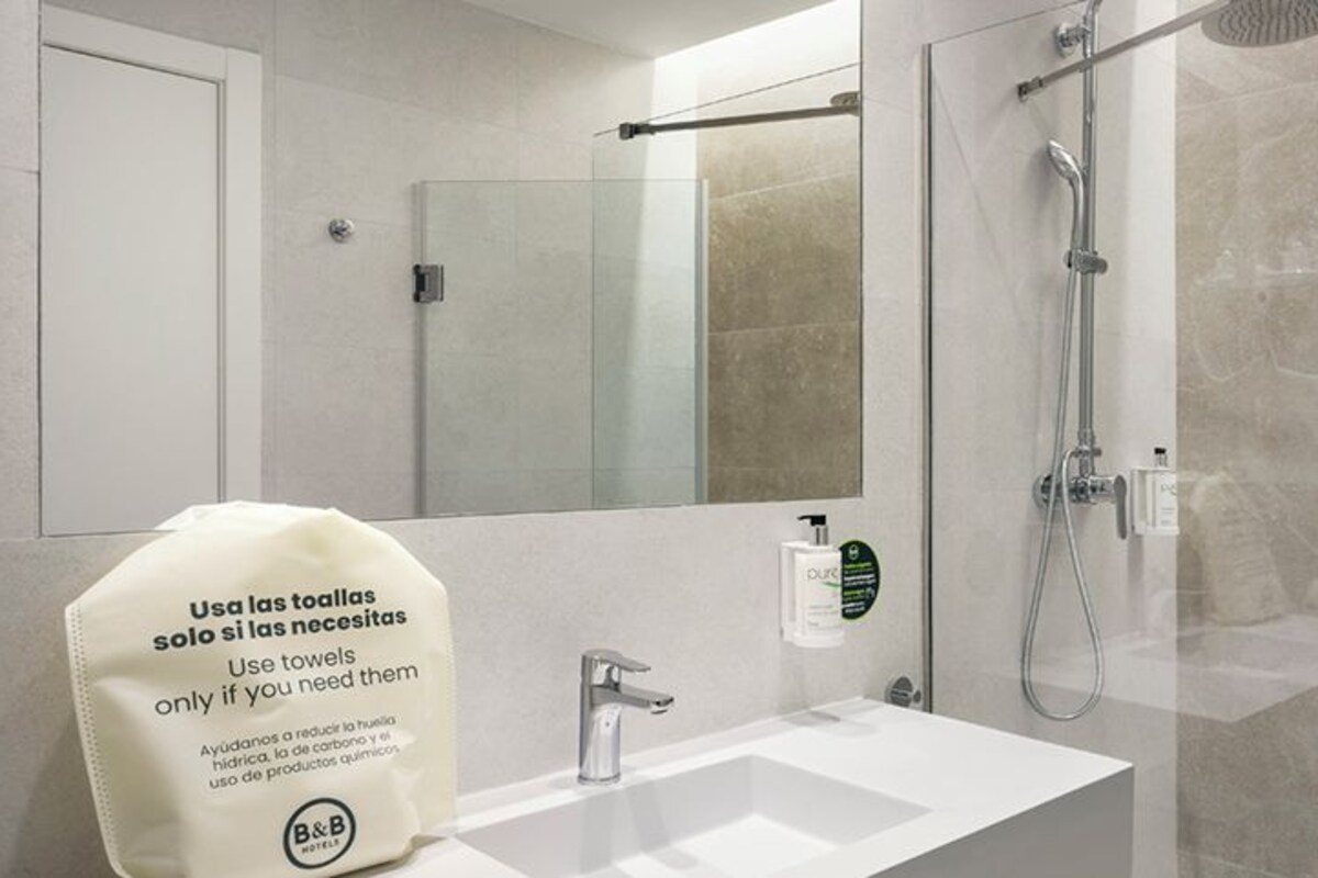 A bathroom with a sink, mirror, shower, and a towel dispenser.