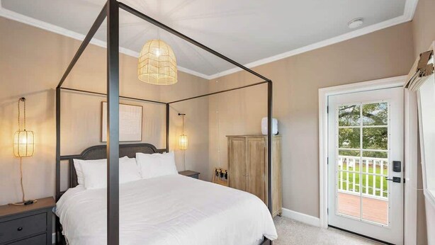 A four-poster bed with a canopy, bedside lamps, a nightstand, a wardrobe, and a door leading to a balcony. - The Cypress Bungalows (Sonoma)