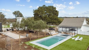 Un jardin avec une piscine, des chaises longues et un espace salon abrité.