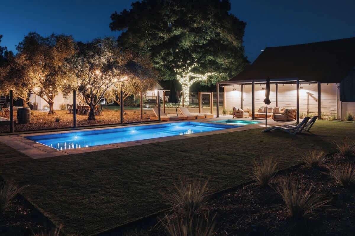 A backyard with a swimming pool, lounge chairs, and a covered seating area.