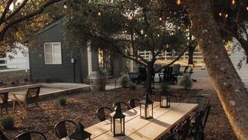 An outdoor dining area with a long wooden table, black chairs, and hanging light fixtures.