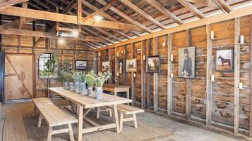 A rustic barn-style interior with wooden beams, a long table with benches, and framed pictures on the walls.