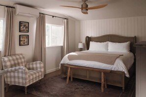 A bedroom with a bed, a chair, a ceiling fan, and a window with curtains.