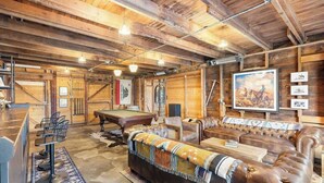 Un intérieur rustique avec un billard, des fauteuils en cuir et des murs en bois.
