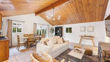 A spacious living area with a high ceiling, wooden beams, a sofa, a coffee table, and a dining set.