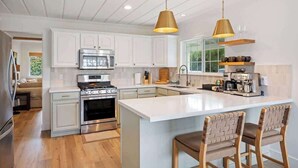 A modern kitchen with white cabinetry, stainless steel appliances, and a central island with bar stools. - The Cypress Bungalows (Sonoma)