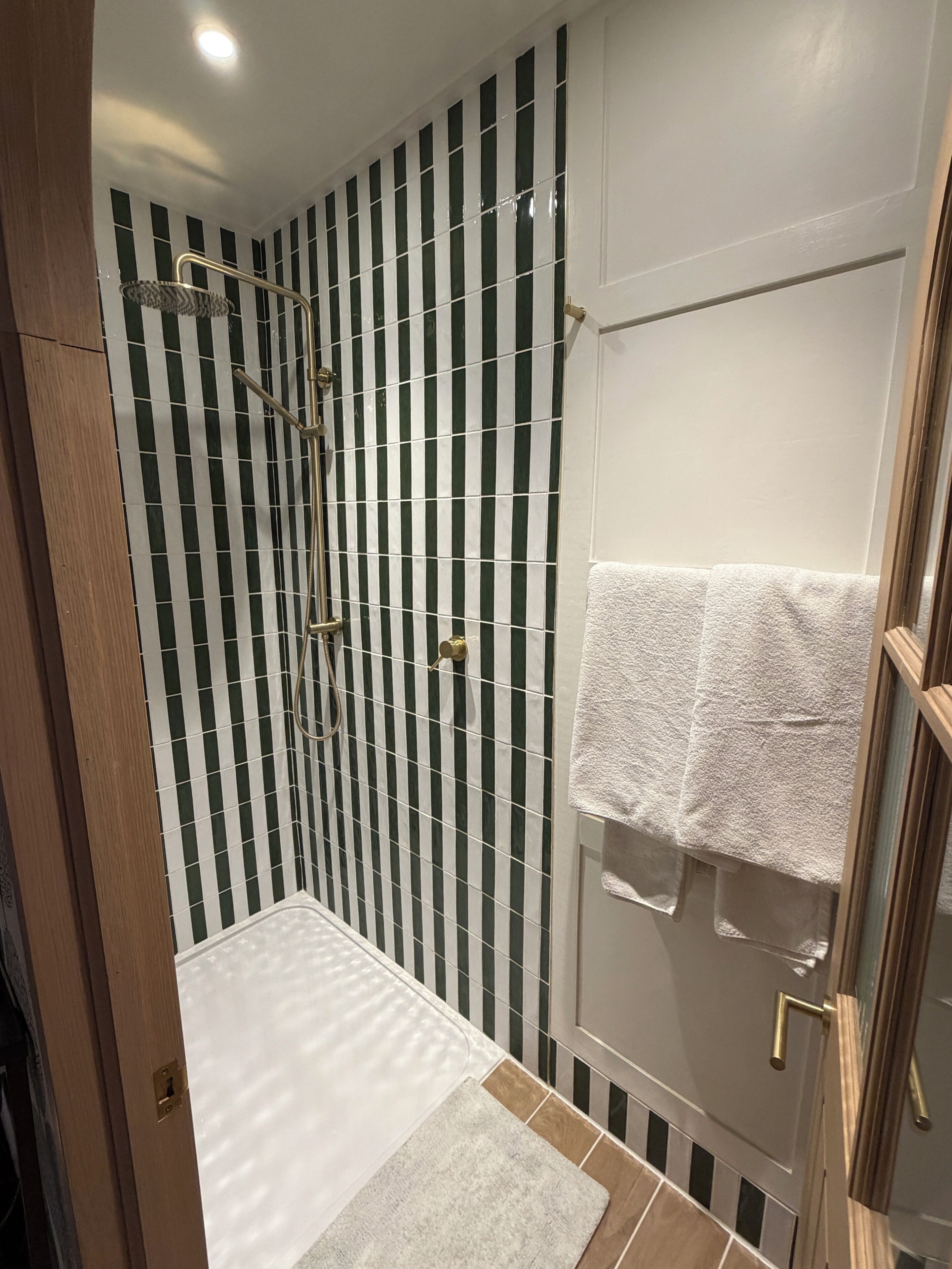 A bathroom with a shower, a towel rack, and a door with a towel hanging on it.