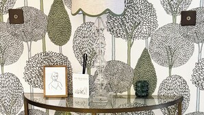 Una habitación con papel tapiz estampado, una mesa con lámpara y obras de arte enmarcadas.