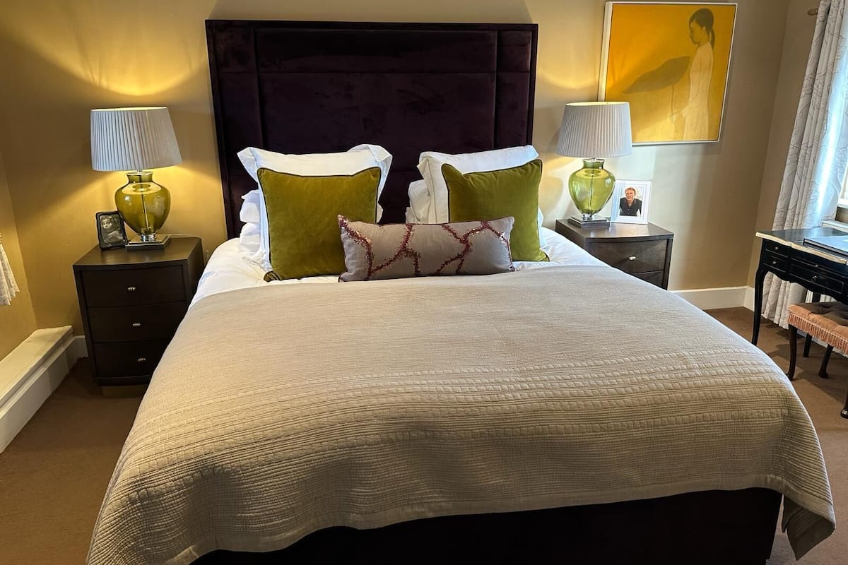 A well-appointed bedroom with a large bed, two bedside tables, a nightstand, a desk, and a chair.