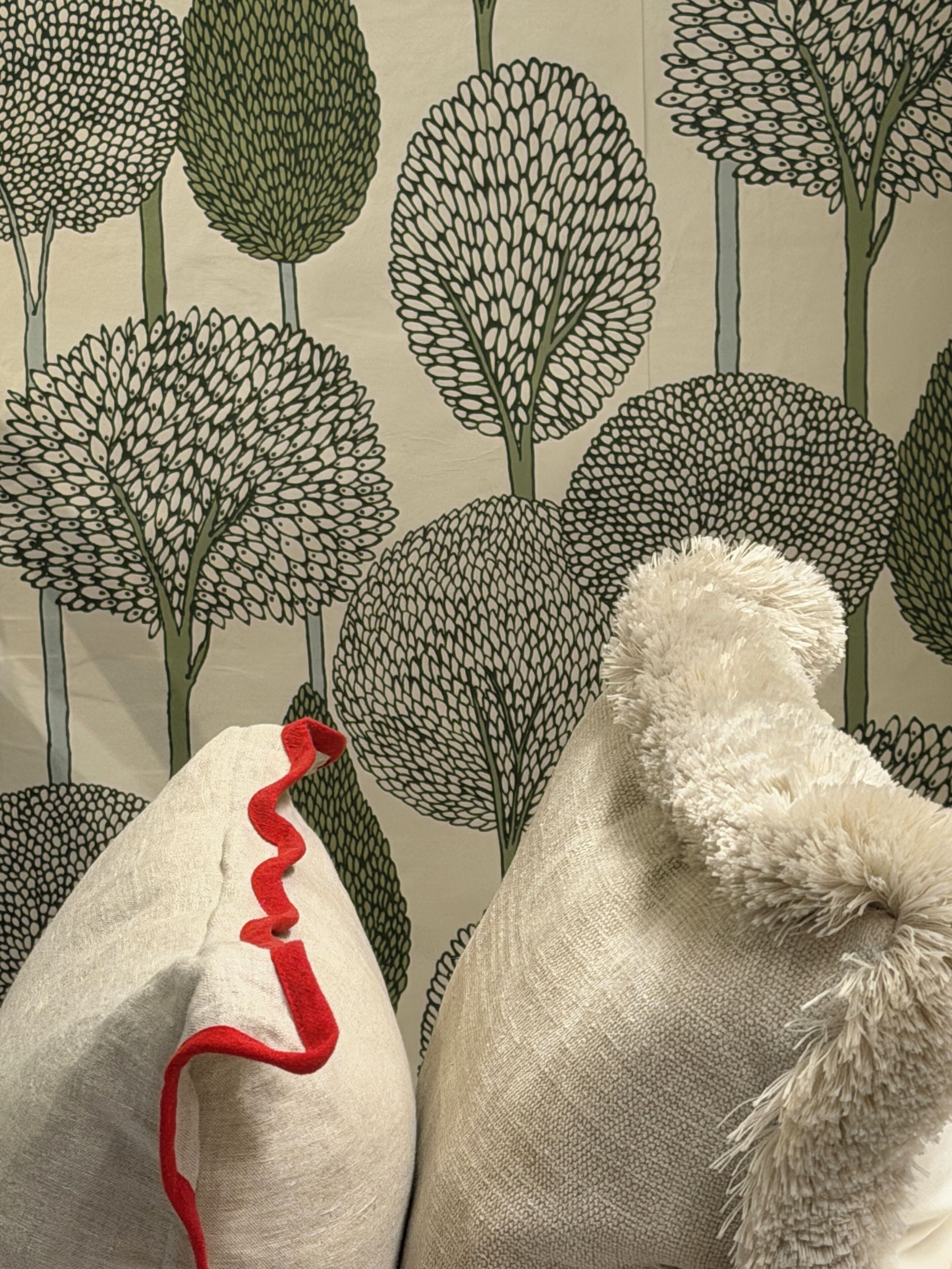 A wall with a pattern of stylized trees and a pillow with a red trim.