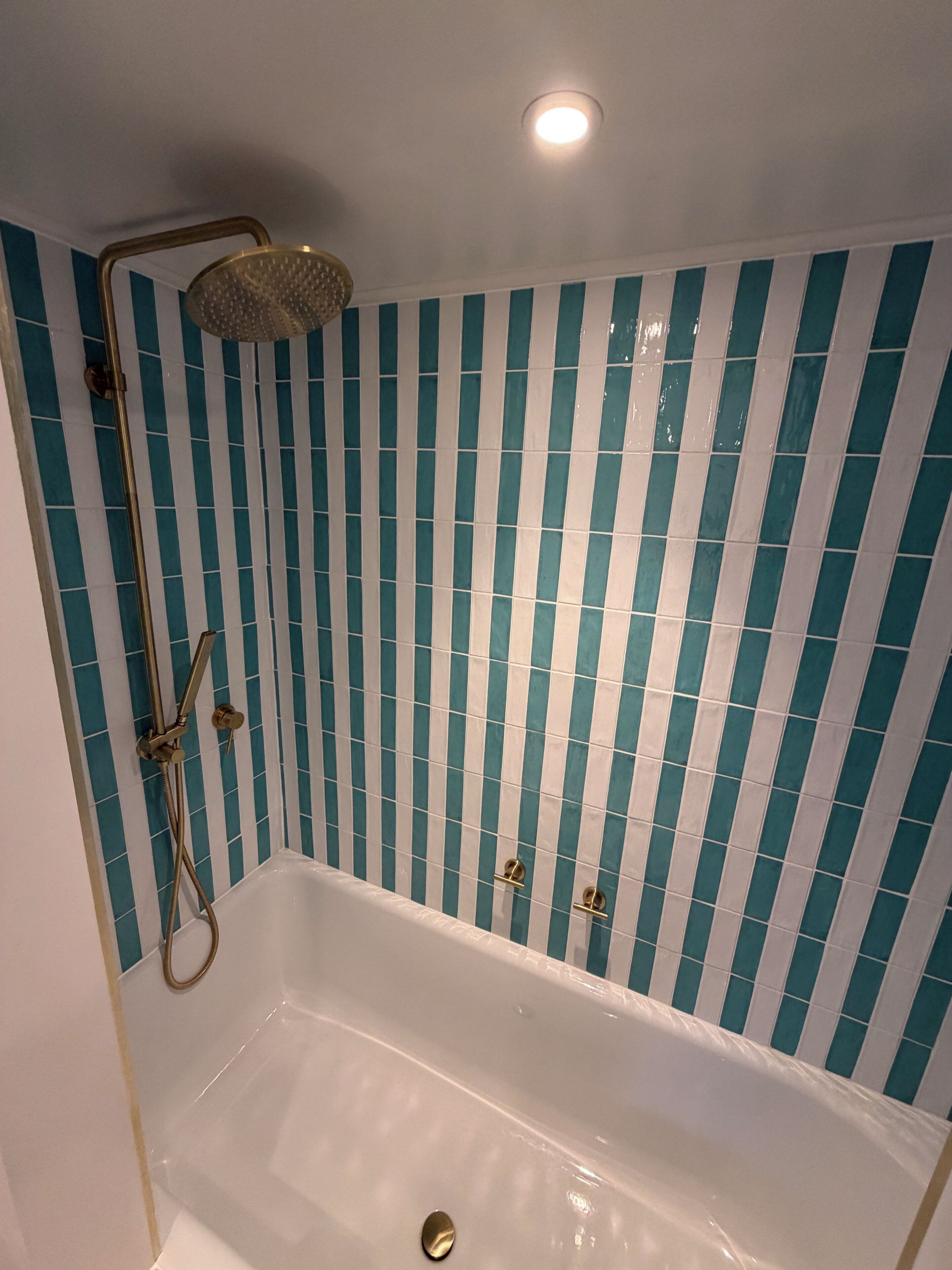 A bathroom with a bathtub, a showerhead, and a tiled wall.