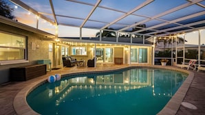 Une piscine avec un patio couvert, un espace salon comprenant un canapé et une table, et une vue sur l’intérieur du bâtiment.