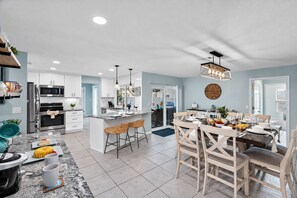Una cocina moderna con una isla central, un comedor con sillas de madera y un reloj grande en la pared.