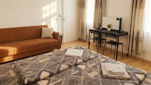 A room with a brown sofa, a patterned bedspread, a desk with a computer, and curtains. - Close to City Center - Affordable Private Rooms with TV (Vienna)