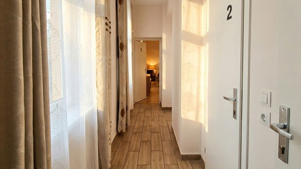 A hallway with wooden flooring, a door with a number, and a room in the distance. - Close to City Center - Affordable Private Rooms with TV (Vienna)