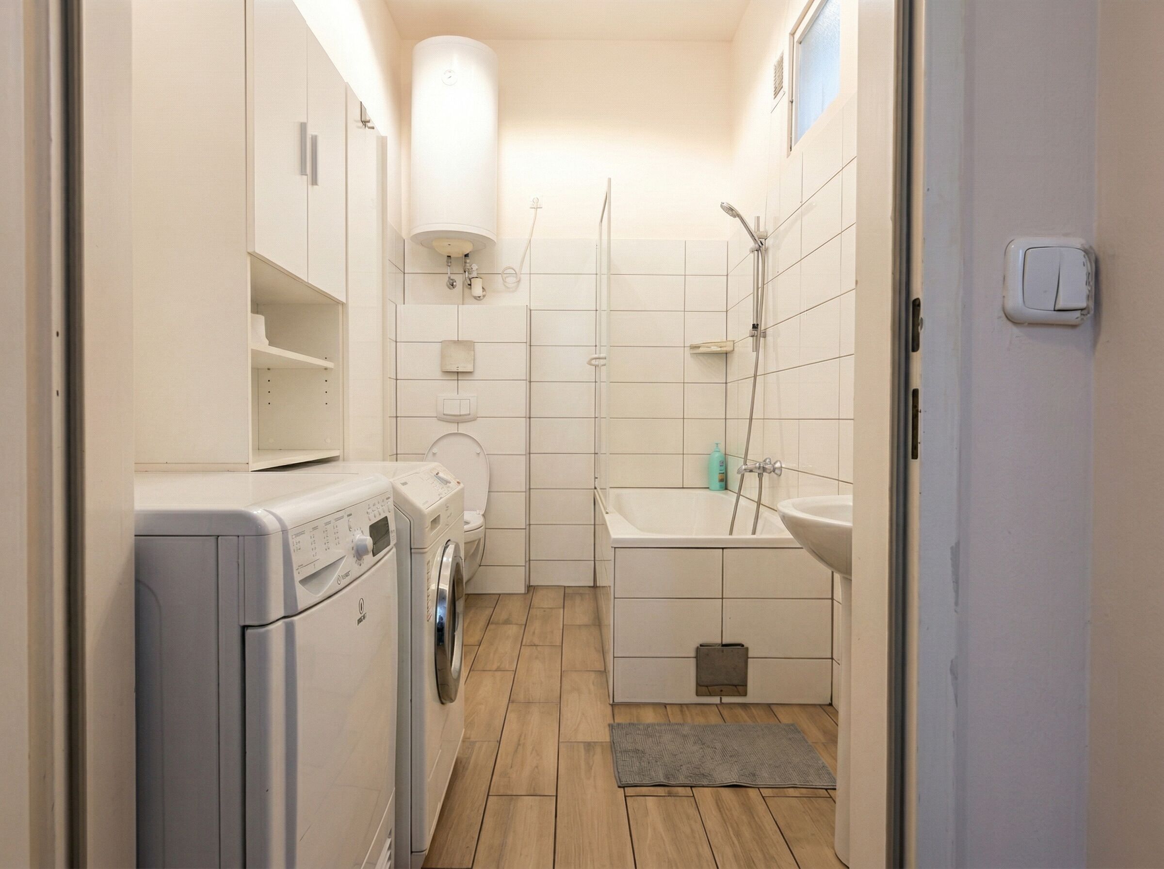 Et lille badeværelse med vaskemaskine, toilet, badekar og håndvask.