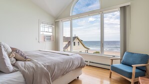 Une chambre avec une grande fenêtre donnant sur la plage, un lit, une chaise et une petite table.