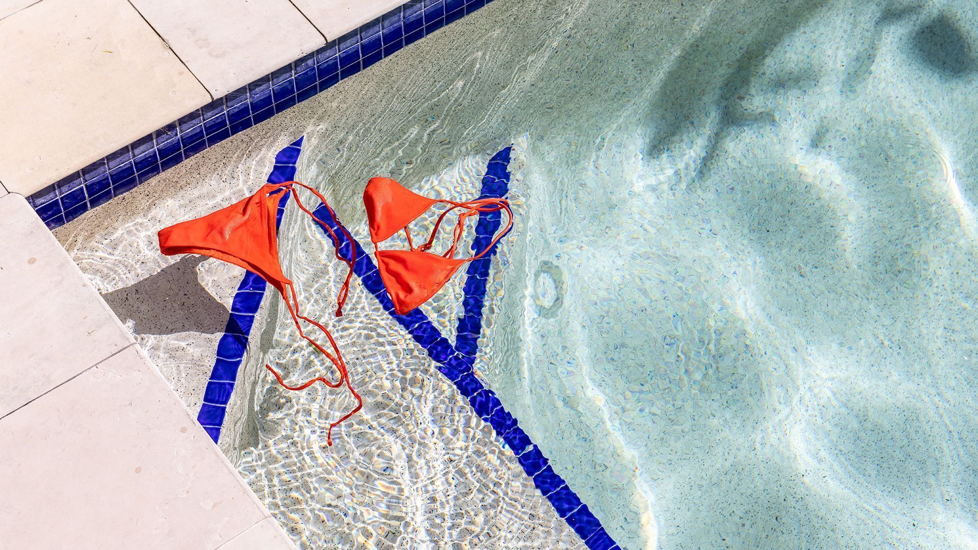 A swimming pool with clear water, blue tiles, and two orange swimwear items.