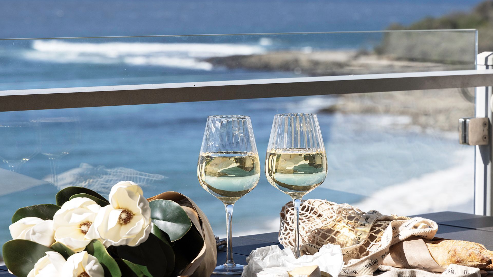 Deux verres de vin blanc sur une table, avec vue sur l’océan.