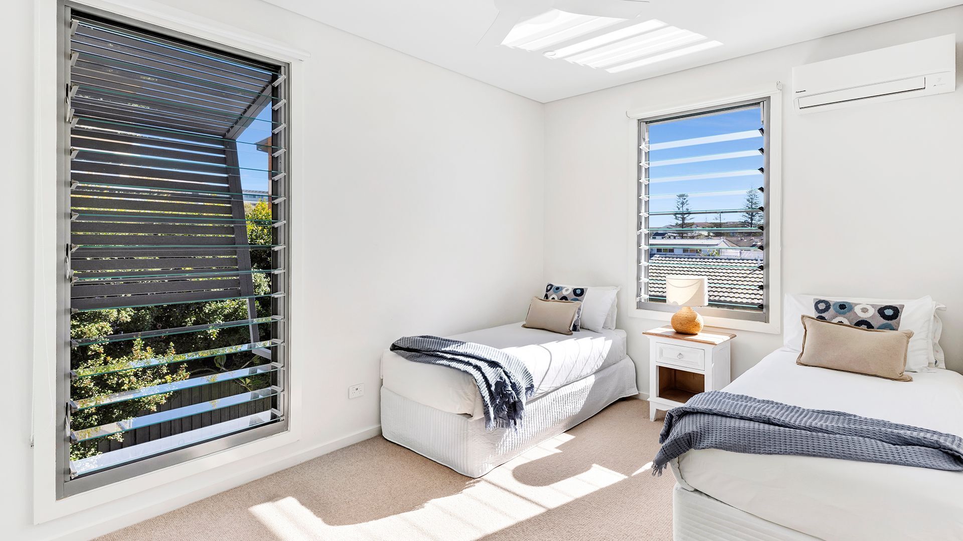 A bedroom with two beds, a nightstand, and a window with blinds.