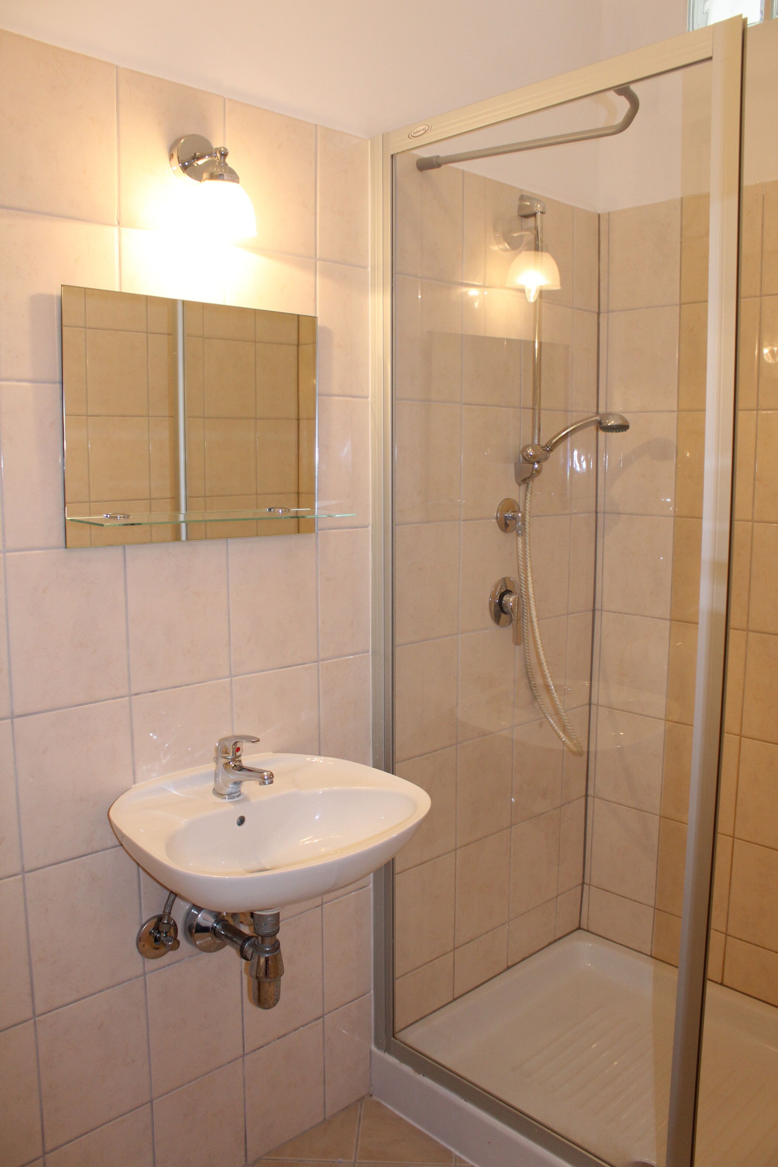 A bathroom with a glass-enclosed shower, a sink with a mirror above it, and tiled walls.