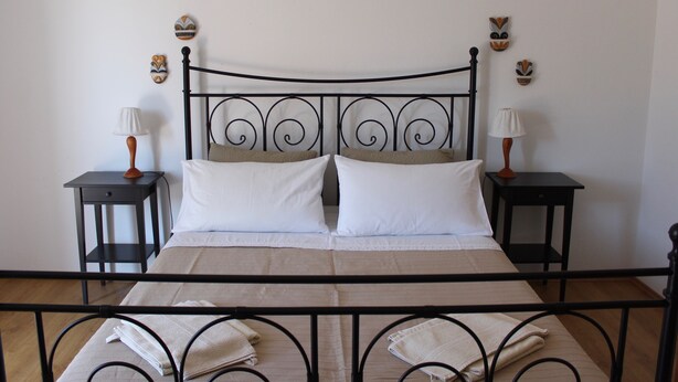 A bed with a black metal frame, two nightstands with lamps, and decorative masks on the wall. - Casa Monte Mulini (Rovinj)