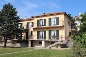 A two-story building with a stone base and a yellow facade, featuring balconies with green shutters and a staircase leading to the entrance. - Casa Monte Mulini (Rovinj)