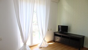 A room with a wooden floor, a dark-colored TV stand, and white curtains. - Casa Monte Mulini (Rovinj)