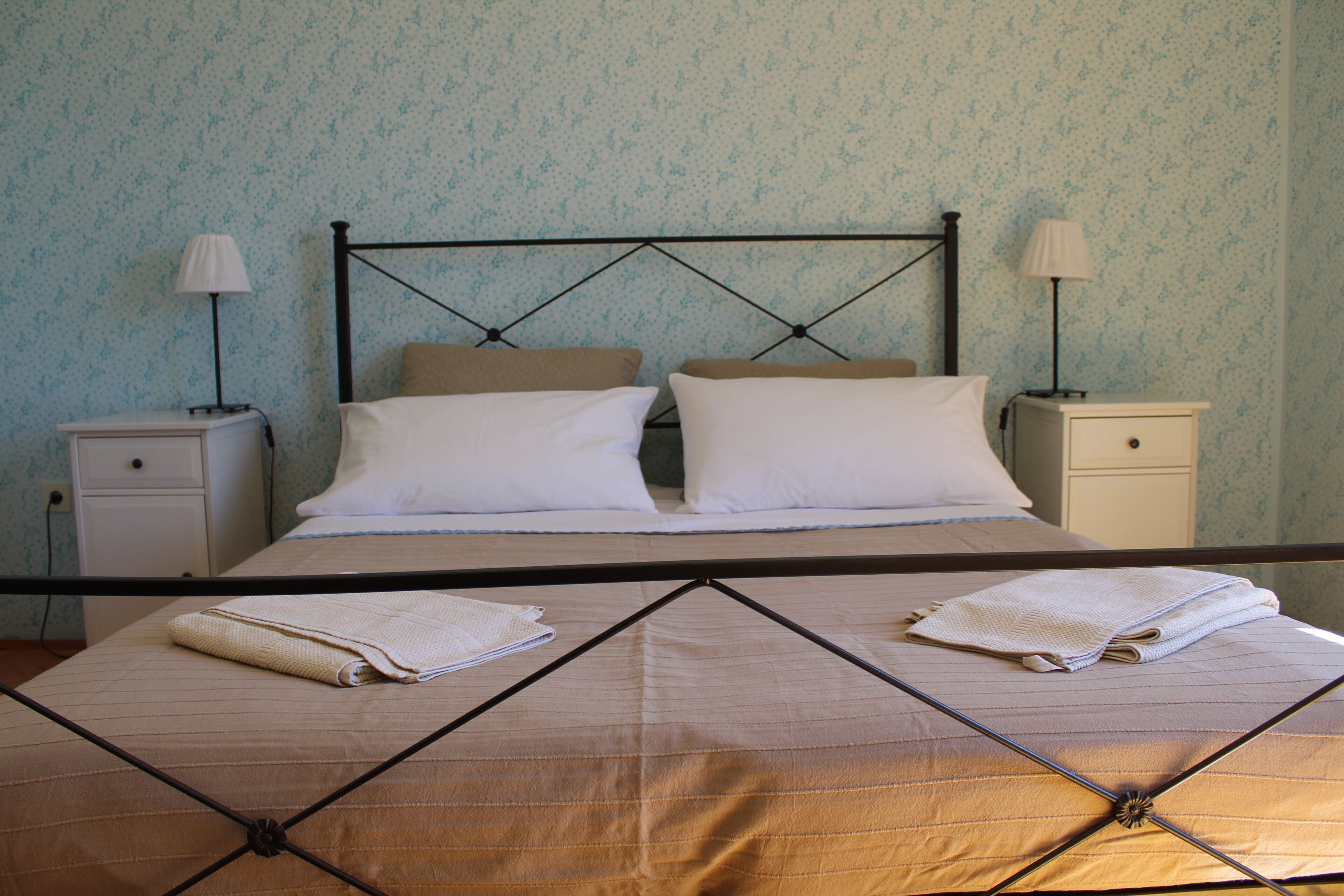 A neatly made bed with a metal frame, two bedside tables with lamps, and a patterned wall.