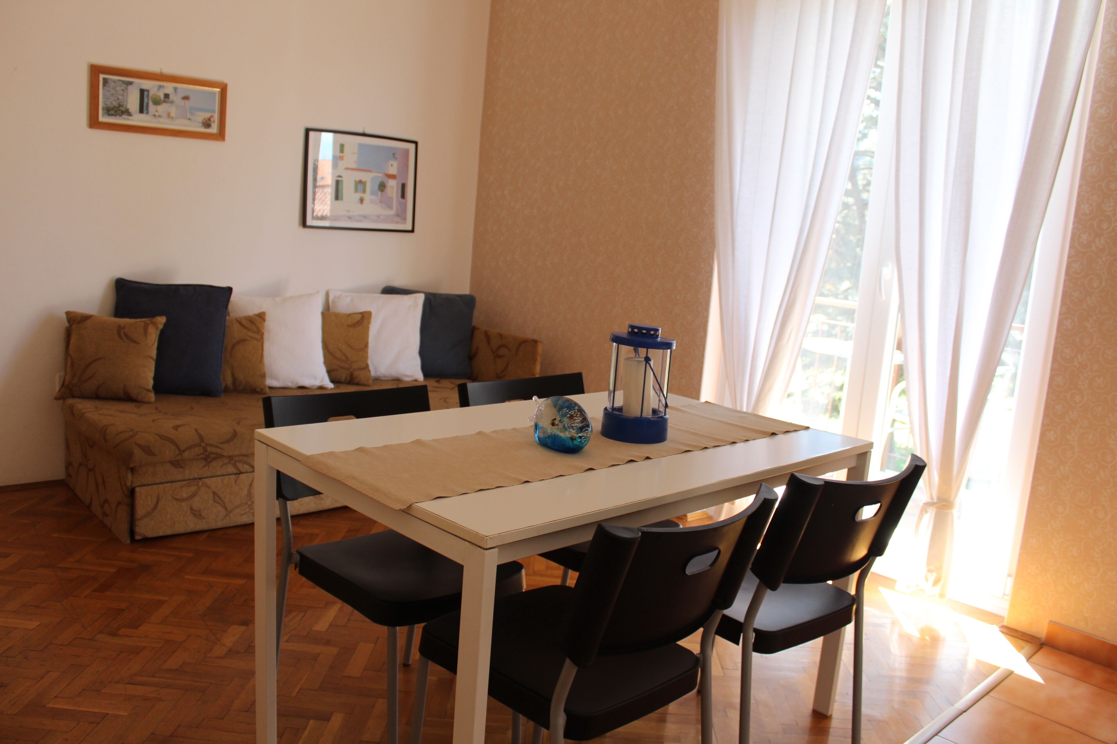 A living room with a sofa, a dining table with chairs, and a window with curtains.