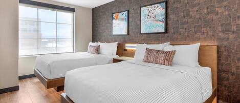 Habitación de hotel con dos camas, un ventanal grande y obras de arte en la pared.