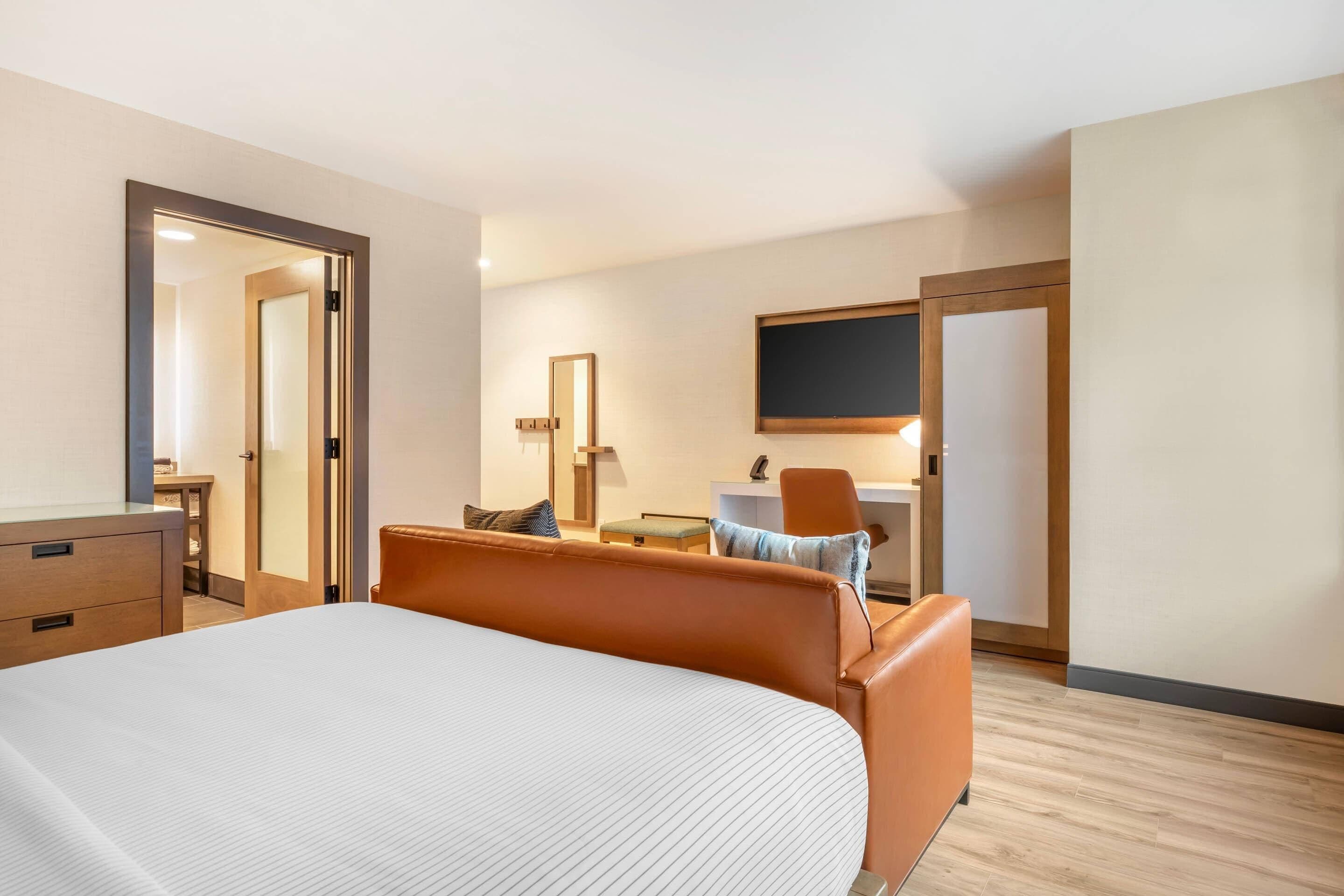 A hotel room with a large bed, a desk, a chair, a TV, and a door.