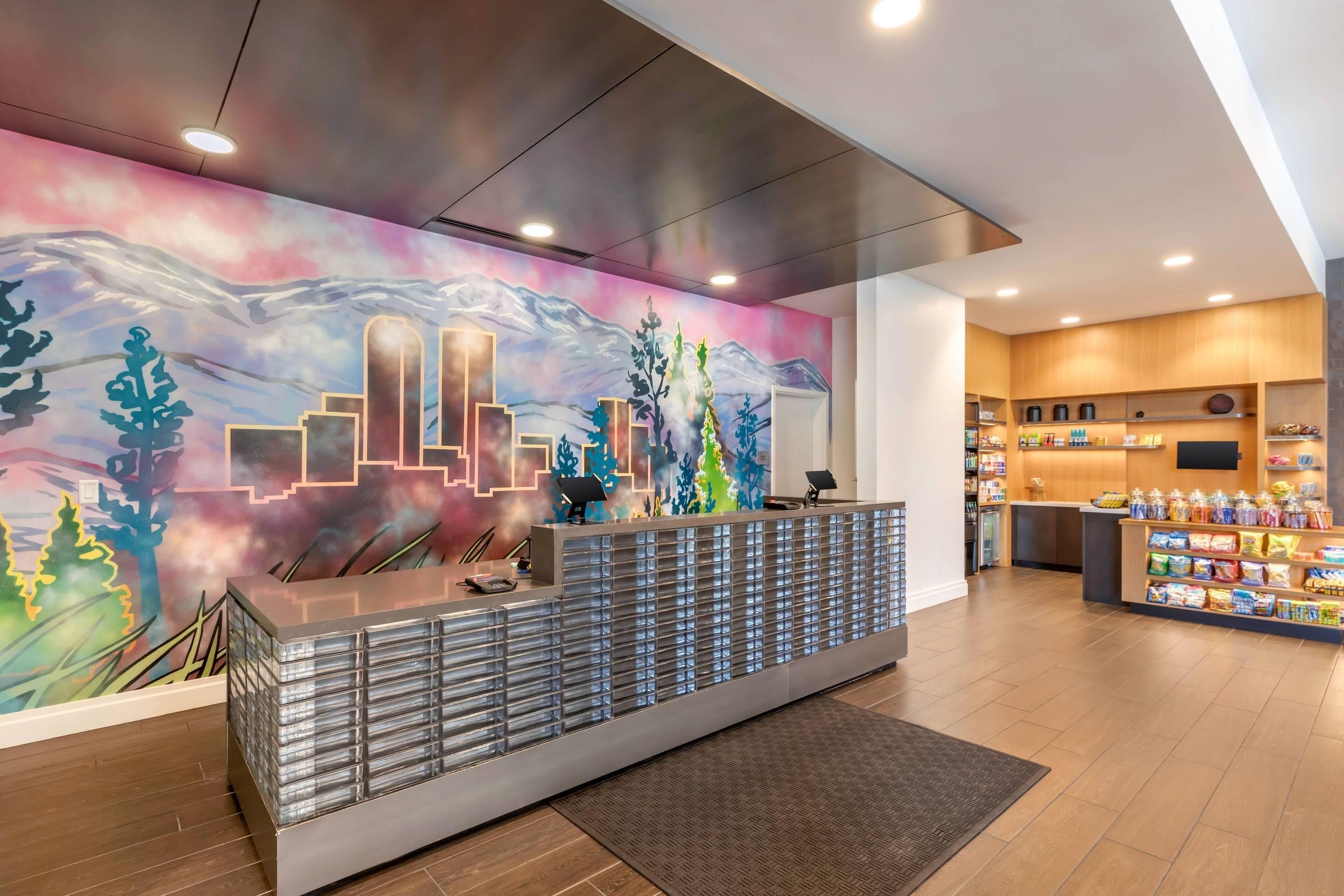 A hotel reception area with a modern design, featuring a reception desk, a wall mural, and a snack bar.