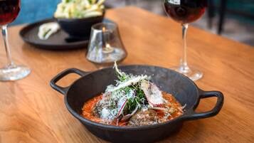 A black cast iron skillet with a dish on a wooden table, accompanied by two glasses of red wine and a small bowl of salad.