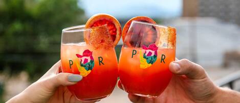 Dos manos sosteniendo vasos con una bebida tropical y una rodaja de fruta decorativa.