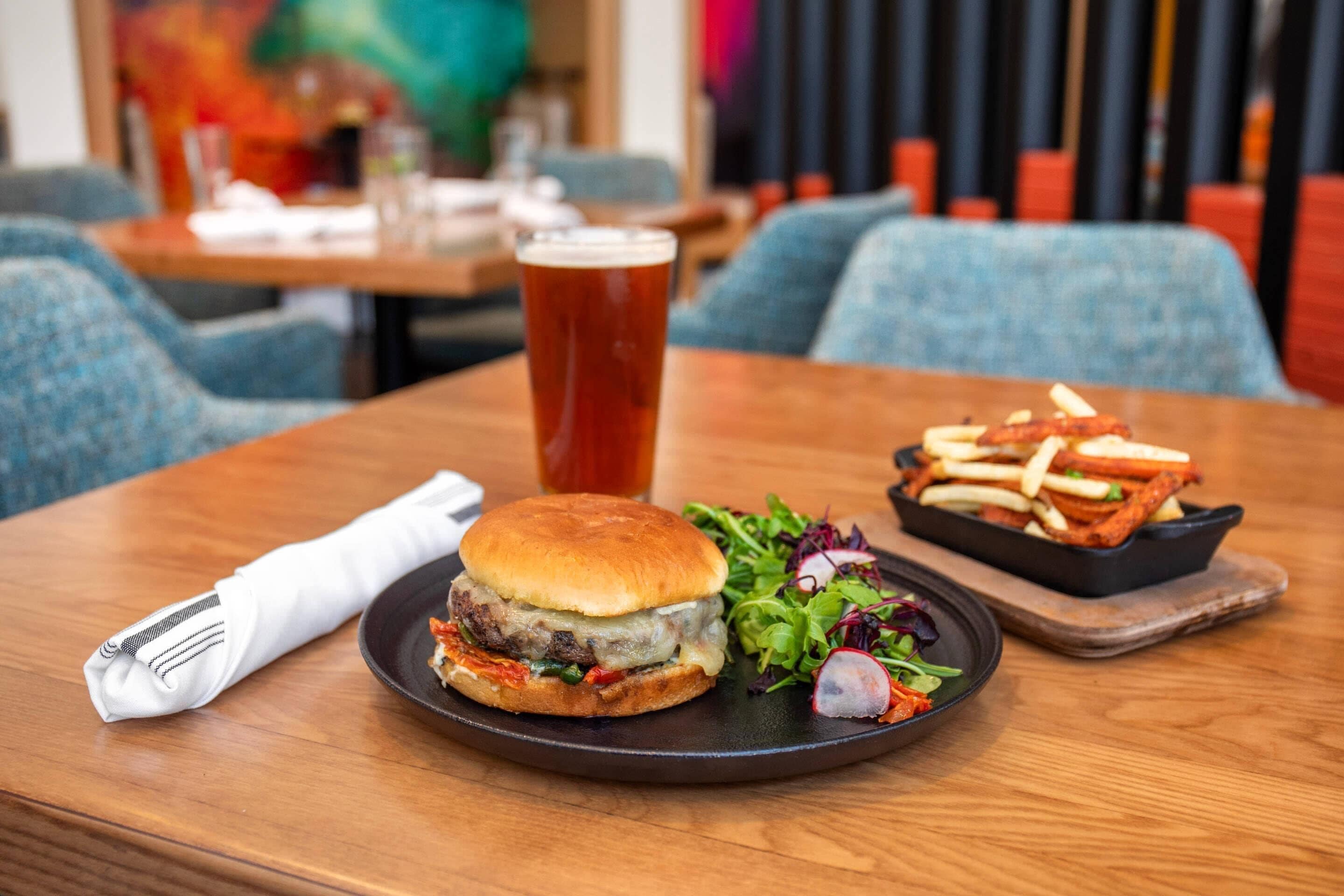 A meal consisting of a burger, fries, and a salad on a wooden table with a napkin and fork on the left.