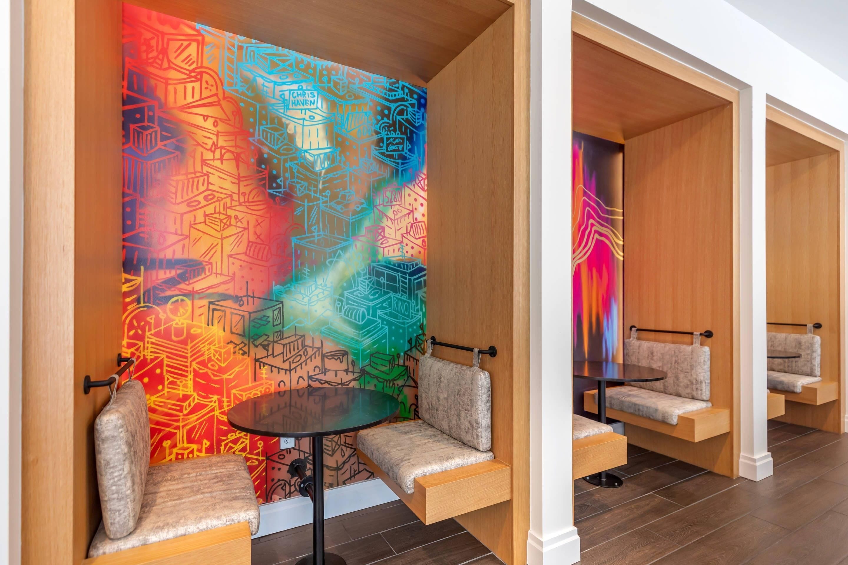 Un interno moderno con un murale geometrico vivace, pannelli in legno e sedute integrate con un piccolo tavolino.